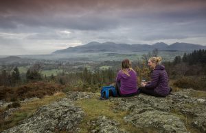 Two females sit on top of an outdoor site looking over the view