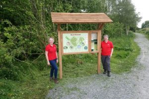 Two staff members stand either side of a map at Glasswater Community Trail.