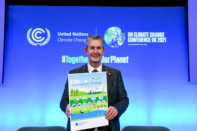 Edwin Poots holding an Environment Strategy poster at COP26