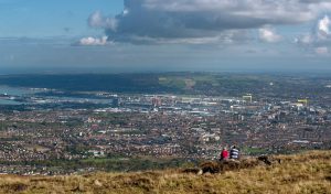 Two people sat at the top of divis mountain looking over the belfast skyline