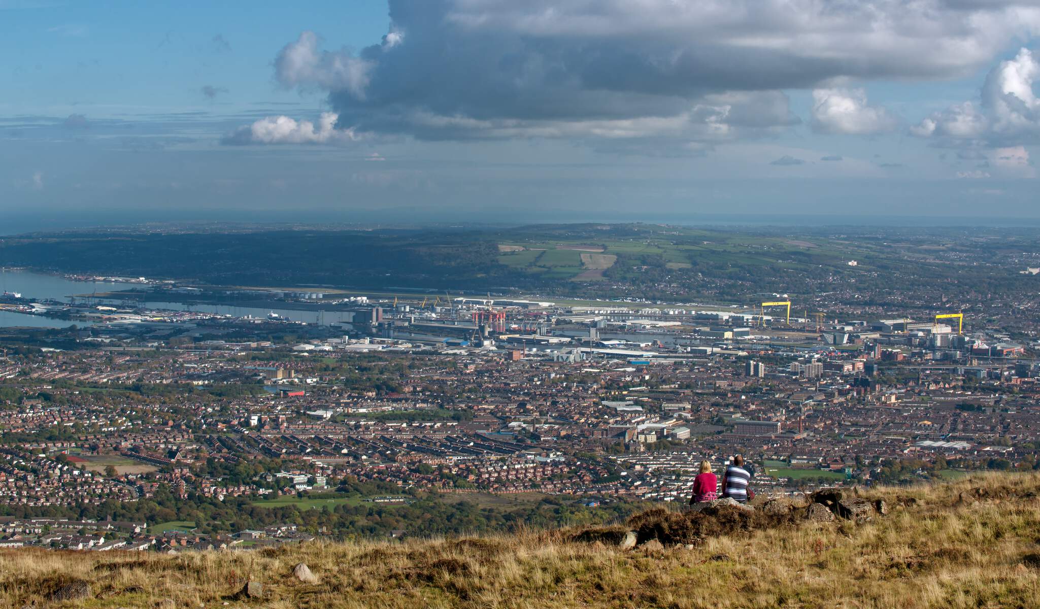 Two people sat at the top of divis mountain looking over the belfast skyline